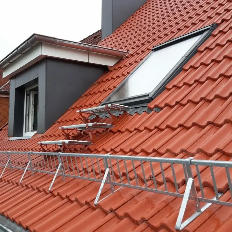 Rotes Ziegeldach mit Dachfenster und montiertem Schneefanggitter